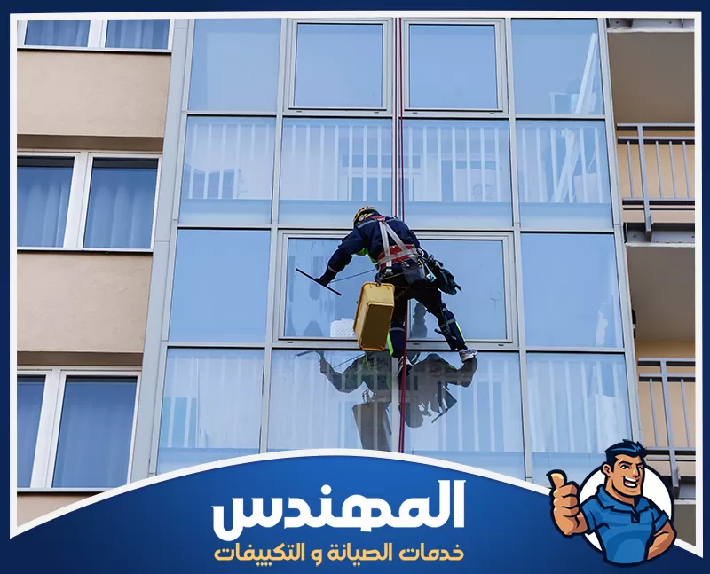تنظيف زجاج السيكوريت بحفر الباطن 0546176127 شركة المهندس رجل ينظف نوافذ مبنى في حفر الباطن، مستخدمًا أدوات خاصة لتنظيف الزجاج الخارجي.