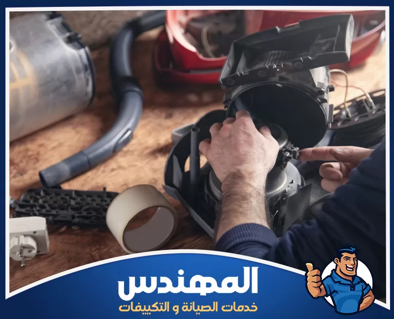 شركة صيانة الاجهزة الكهربائية بحفر الباطن 0546176127 المهندس للصيانة صيانة داخلية لجهاز مكنسة كهربائية بعد فتح الهيكل، حيث يعمل على فحص المحرك والأجزاء الداخلية بدقة على طاولة العمل، مع وجود خرطوم المكنسة وقطعها المفككة وأدوات الصيانة حوله، في مشهد يوضح عملية إصلاح وتنظيف شاملة للجهاز.