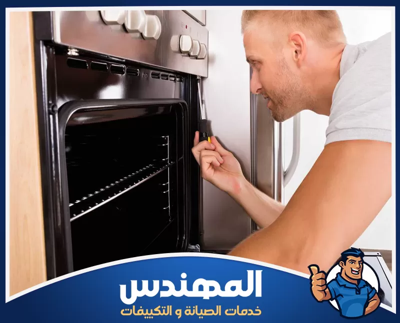 الأجهزة المستخدمة في شركة صيانة افران بحفر الباطن 0546176127 المهندس فني يفحص باب فرن منزلي ويعمل على إصلاح المفصلات باستخدام مفك يدوي.