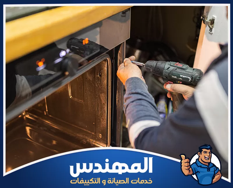 شركة صيانة افران بحفر الباطن 0546176127 المهندس فني يصلح باب فرن منزلي باستخدام مثقاب كهربائي أثناء أعمال الصيانة.
